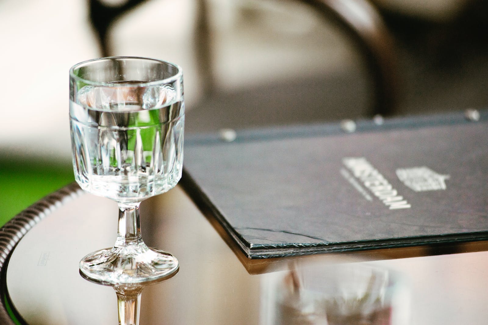 Verre d'eau élégant en cristal sur une table brillante, avec un menu flou marqué "AMSTERDAM" en arrière-plan. Ambiance rafraîchissante.